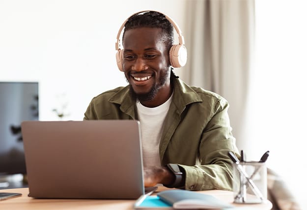 Man with headphones smiling while listening to a science of reading podcast and using a laptop at a desk.