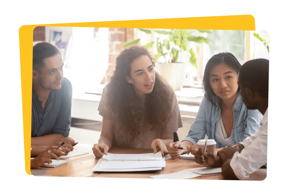 Group of four diverse colleagues discussing over documents at a table in a brightly lit office.